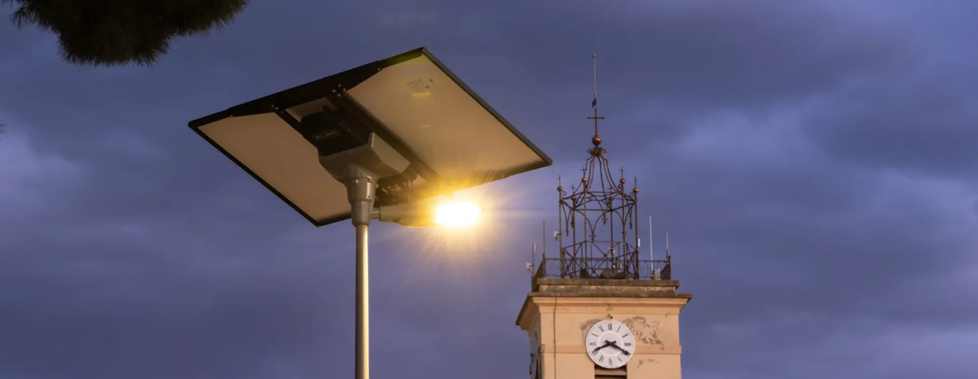Mât d’éclairage solaire allumé au crépuscule devant le clocher de l’église de La Crau (Var)