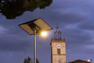 Mât d’éclairage solaire allumé au crépuscule devant le clocher de l’église de La Crau (Var)