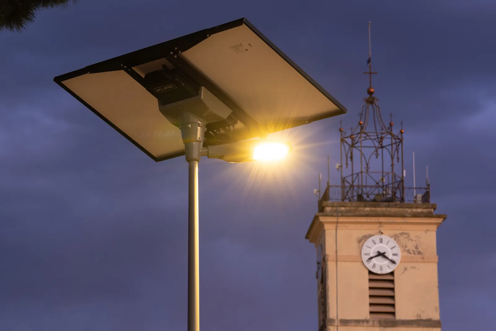 Mât d’éclairage solaire et clocher de l’église au crépuscule, à La Crau (Var)